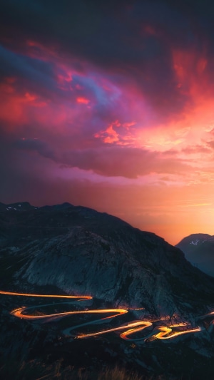 Mountain road with car light trails at sunset