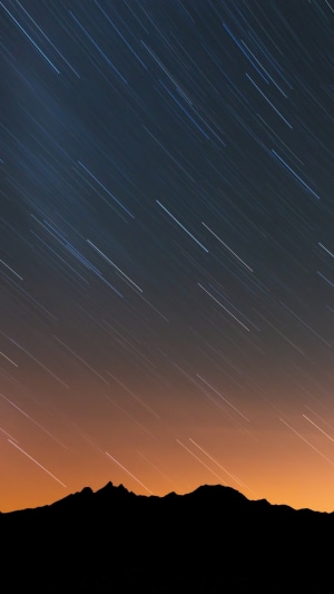 Star trails over silhouetted mountains at night