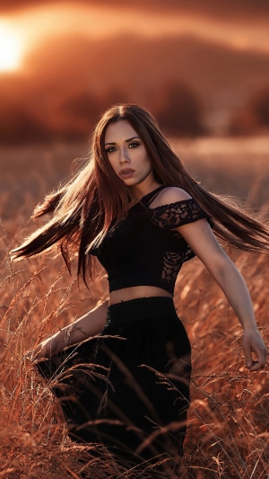 Woman in black dress in a field at sunset
