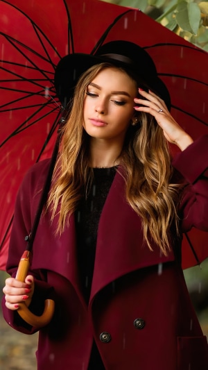 Woman in hat holding red umbrella in rain