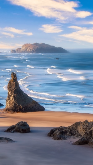 Ocean waves crash on a rocky beach with islands in the distance