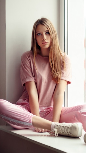 Young woman in pink loungewear sitting by window