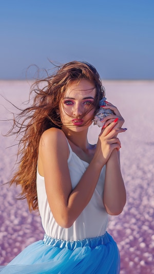 Model holding seashell on pink salt flats