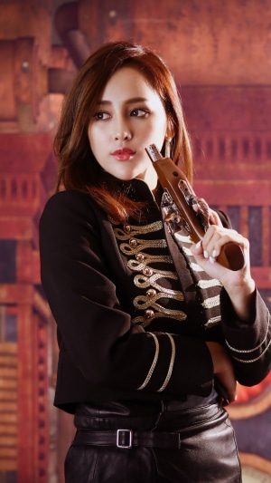 Woman in black military-style jacket holding a pistol