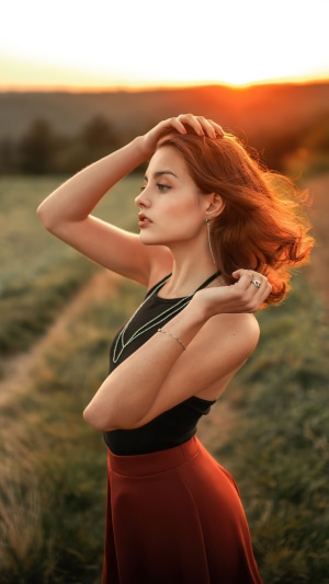 Young woman with red hair in a field at sunset