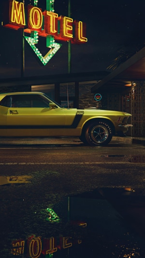 Yellow Ford Mustang parked at a motel at night