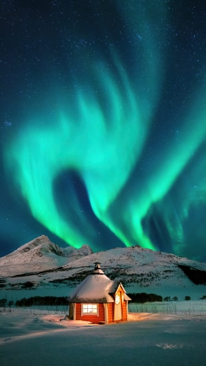 Aurora Borealis over snowy mountains and a cabin
