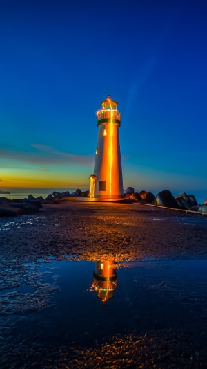 Lighthouse illuminated at dusk with reflection