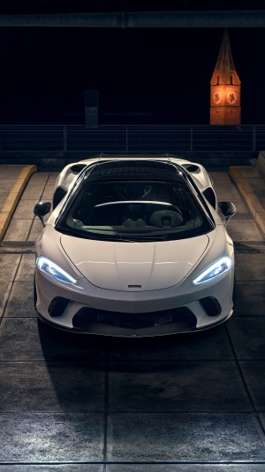 White McLaren GT parked at night with church tower