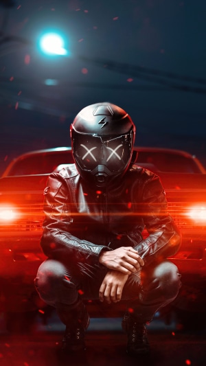 Man in helmet and leather jacket crouching in front of car