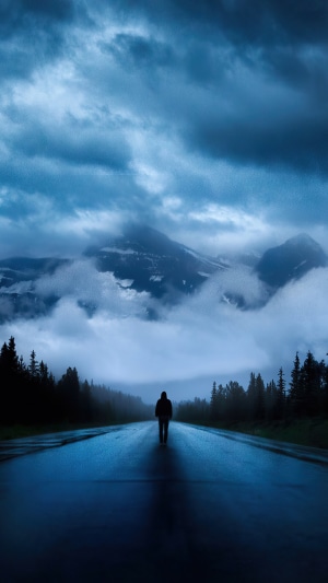 Person walking on a wet road towards mountains