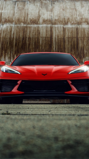 Red Chevrolet Corvette C8 parked in front of a corrugated metal wall