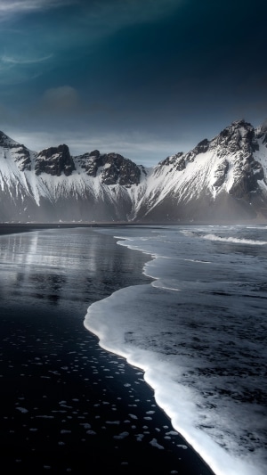 Snow-capped mountains and black sand beach with waves