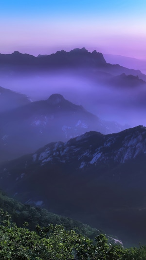 Mountains shrouded in purple mist under a blue and purple sky