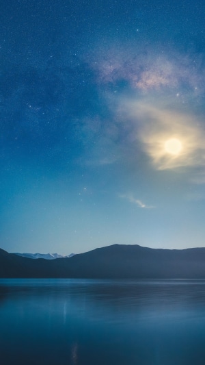 Lake under starry sky with moon and mountains