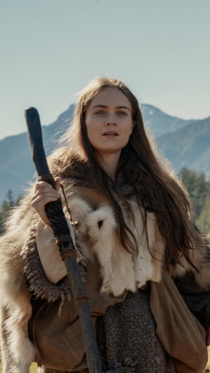 Woman in fur holding a staff in front of mountains