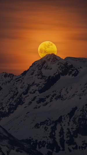 Full moon rising over snow-capped mountains at sunset