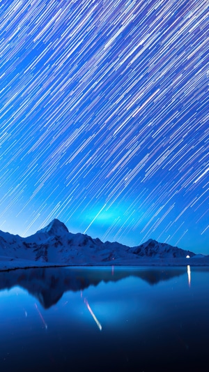 Star trails over snowy mountains and lake