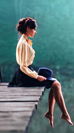 Woman in yellow blouse and black skirt sitting on a dock