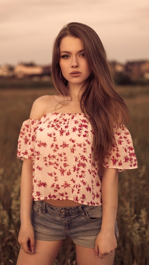 Woman with long brown hair wearing a floral top and denim shorts