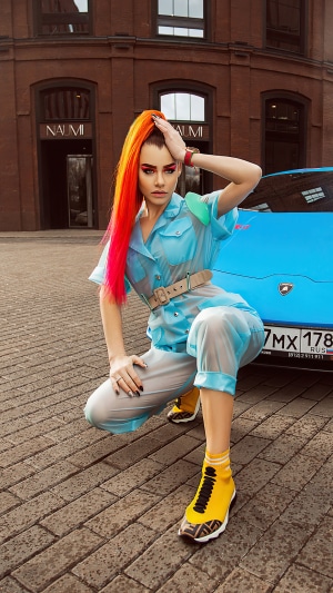 Woman with bright hair and blue outfit next to a Lamborghini