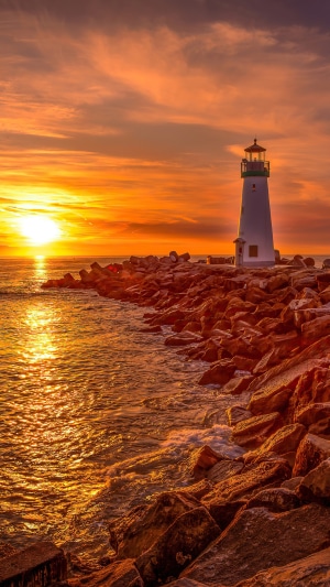 Lighthouse on rocky shore at sunset 4K