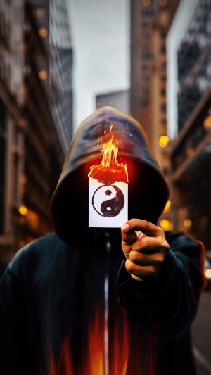 Person in hoodie holding burning yin yang card