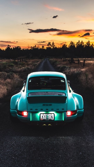 Rear view of a teal Porsche 911 on a dirt road at sunset