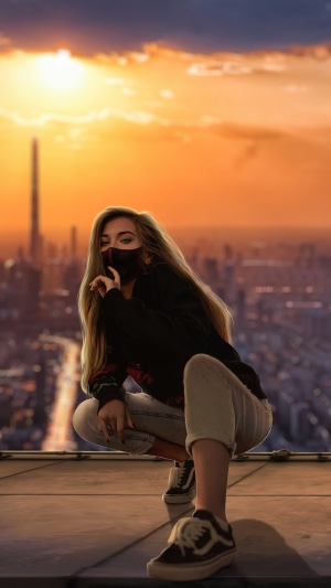 Woman wearing a mask crouching on a rooftop at sunset