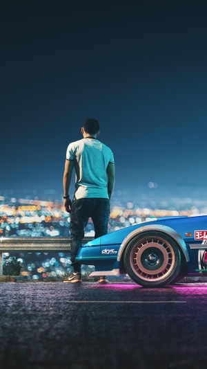 Man standing next to a blue car overlooking a city at night