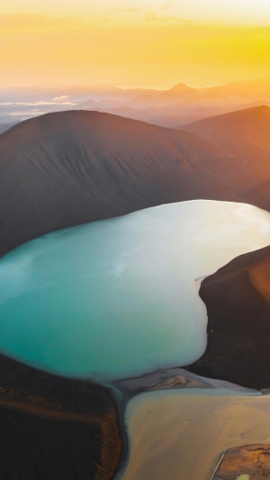 Turquoise lake surrounded by dark volcanic mountains at sunset 4K