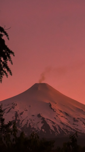 Snow-capped volcano emitting smoke at sunset