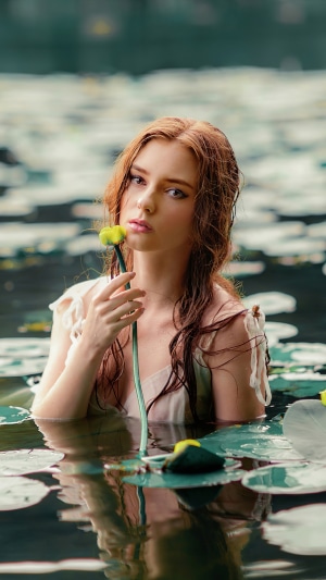 Young woman with red hair in water holding a flower