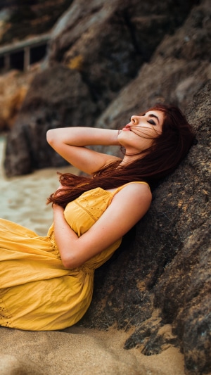 Woman in yellow dress leaning against rocks on a beach