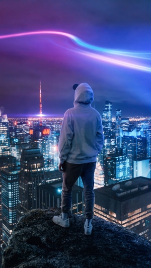 Person in hoodie overlooking neon city at night