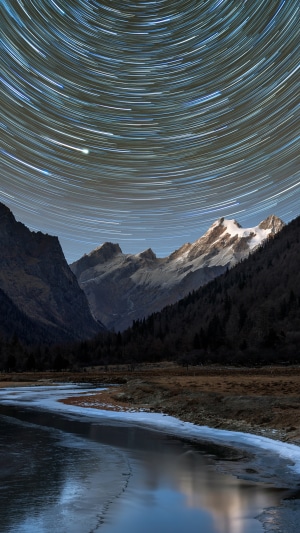 Star trails over snowy mountains and river