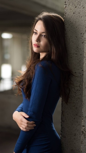 Woman in blue dress leaning against concrete pillar