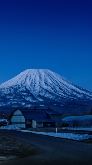 Snow-covered mountain and farm buildings under a clear blue sky