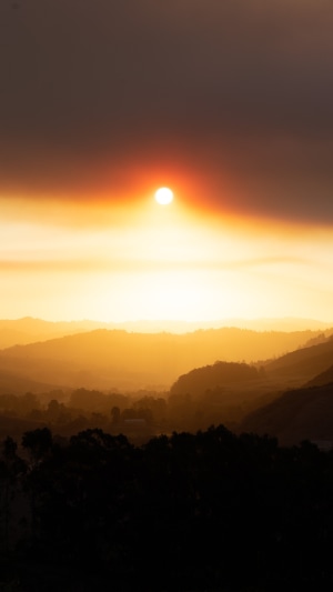 Sun obscured by smoke over rolling hills