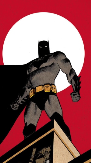Batman standing on a rooftop with a large moon behind him