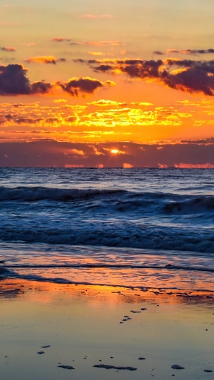 Sunrise over the ocean with clouds and waves