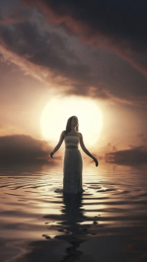 Woman standing in water at sunset