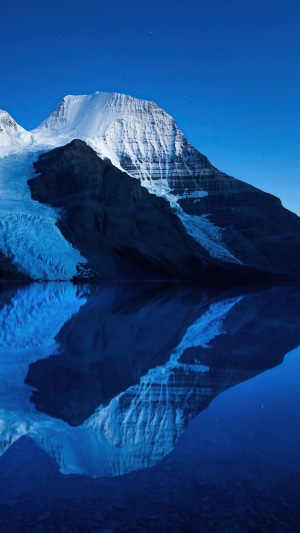 Snow-capped mountain reflected in calm water under a starry night sky