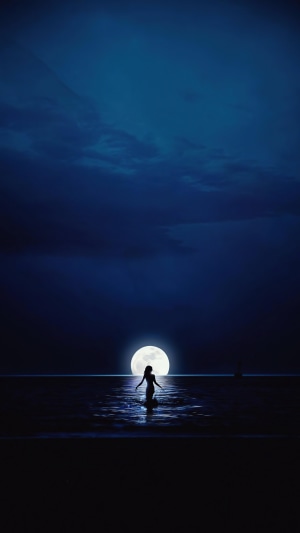 Silhouette of a person in the ocean under a full moon