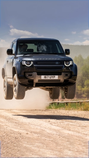 Black Land Rover Defender jumping over dirt road 4K