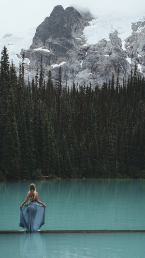 Woman in a blue dress on a log in a lake with mountains