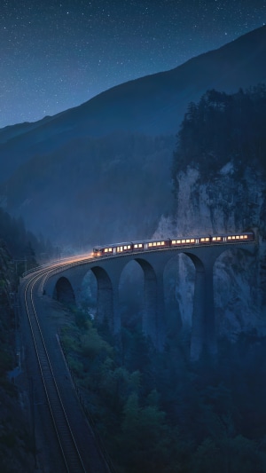 Train crossing a bridge in mountains at night 4K