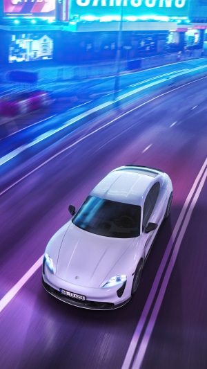 White Porsche Taycan Turbo S driving on a neon-lit road