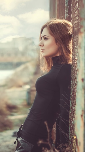 Girl in black turtleneck dress leaning against fence