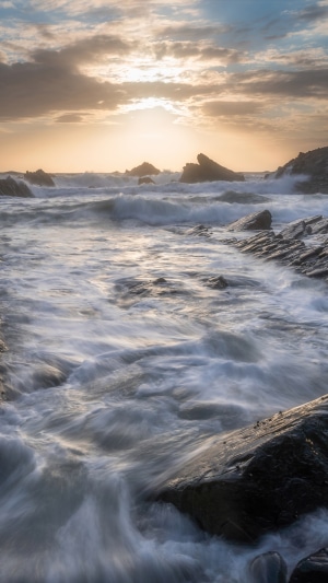 Waves crashing on rocky beach at sunset 4K